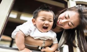 Chinese mother bending forward while holding her baby playfully and they are both smiling 